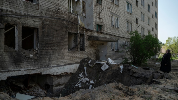 FILE - A woman stand next to a crater from an explosion that damaged an apartment and a basement of a residential building killing, according to the residents, a 8-year-old girl during a Russian attack yesterday in Lyman, Ukraine, Tuesday, April 26, 2022. (AP Photo/Leo Correa)