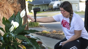 Kayla Kelly grieves as mourners gather and lay flowers and gifts at the site of a deadly car crash during an impromptu memorial service on Sunday, Oct. 2, 2022, in Lincoln, Neb. Police in Nebraska said a passenger’s cellphone automatically alerted responders after a car hit the tree in a crash that killed all of its young occupants. (Kenneth Ferriera/Lincoln Journal Star via AP)
