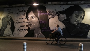 A woman rides bicycle front of a mural signed by Clacks-one and Heartcraft_Street art, depicting women cutting their hair to show support for Iranian protesters standing up to their leadership over the death of a young woman in police custody, in a tunnel in Paris, France, Wednesday, Oct. 5, 2022. (AP Photo/Francois Mori)