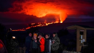 People pose for a photo in front of lava erupting from Hawaii's Mauna Loa volcano Wednesday, Nov. 30, 2022, near Hilo, Hawaii. (AP Photo/Gregory Bull)