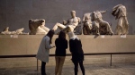 FILE - Women stand by a marble statue of a naked youth thought to represent Greek god Dionysos, center, from the east pediment of the Parthenon, on display during a media photo opportunity to promote a forthcoming exhibition on the human body in ancient Greek art at the British Museum in London, Thursday, Jan. 8, 2015. (AP Photo/Matt Dunham, File)