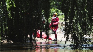 A rescue worker stands next to a body retrieved from the Jukskei river in Johannesburg, Sunday, Dec. 4, 2022. At least nine people have died while eight others are still missing in South Africa after they were swept away by a flash flood along the Jukskei river in Johannesburg, rescue officials said Sunday. (AP Photo)