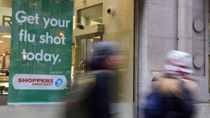 People walk past a sign for flu shots in Toronto on Jan. 9, 2018. THE CANADIAN PRESS/Doug Ives 