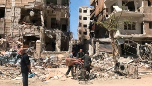 People stand in front of damaged buildings, in the town of Douma, the site of a suspected chemical weapons attack, near Damascus, Syria, Monday, April 16, 2018. A report published Friday, Jan. 27, 2023, by a team from the Organization for the Prohibition of Chemical Weapons established there are â€œreasonable grounds to believeâ€ Syria's air force dropped two cylinders containing chlorine gas on the city of Douma in April 2018, killing 43 people. (AP Photo/Hassan Ammar, File)