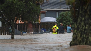 Emergency workers and a man wade through flood waters in Auckland, New Zealand, Friday, Jan. 27, 2023. Torrential rain and wild weather in Auckland causes disruptions throughout the city and an Elton John concert to be canceled just before it was due to start. (Hayden Woodward/New Zealand Herald via AP)