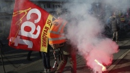 Demonstrator of the CGT union wearing a railway worker jacket holds a flare during a protest march, in Bayonne, southwestern France, Tuesday, Jan. 31, 2023. French labor leaders hope to bring more than 1 million demonstrators into the streets again in the latest clash of wills with the government over plans to push back France's retirement age. (AP Photo/Bob Edme)