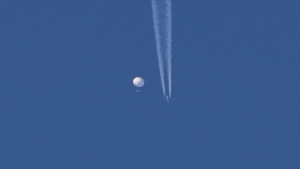 In this photo provided by Brian Branch, a large balloon drifts above the Kingston, N.C. area, with an airplane and its contrail seen below it. The United States says it is a Chinese spy balloon moving east over America at an altitude of about 60,000 feet (18,600 meters), but China insists the balloon is just an errant civilian airshipÂ used mainly for meteorological research that went off course due to winds and has only limited 'self-steering' capabilities. (Brian Branch via AP)