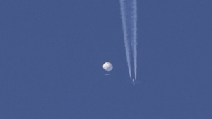 In this photo provided by Brian Branch, a large balloon drifts above the Kingston, N.C. area, with an airplane and its contrail seen below it. The United States says it is a Chinese spy balloon moving east over America at an altitude of about 60,000 feet (18,600 meters), but China insists the balloon is just an errant civilian airshipused mainly for meteorological research that went off course due to winds and has only limited “self-steering” capabilities. (Brian Branch via AP)