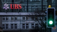 A traffic light signals green in front of the logos of the Swiss banks Credit Suisse and UBS in Zurich, Switzerland, Sunday March 19, 2023. (Michael Buholzer/Keystone via AP)