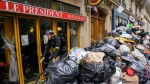 A cyclist rides past an uncollected garbage pile next to the cafe "The President" in Paris, Tuesday, March 21, 2023. The bill pushed through by President Emmanuel Macron without lawmakers' approval still faces a review by the Constitutional Council before it can be signed into law. Meanwhile, oil shipments in the country were disrupted amid strikes at several refineries in western and southern France. (AP Photo/Michel Euler)