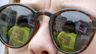 Demonstrators are reflected in the glasses of a participant in Halle/Saale, Germany, Thursday, March 23, 2023. German unions are calling on thousands of workers across the country's transport system to stage a one-day strike on Monday that is expected to bring widespread disruption to planes, trains and local transit. (Hendrik Schmidt/dpa/dpa via AP)