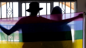 A gay Ugandan couple cover themselves with a pride flag as they pose for a photograph in Uganda Saturday, March 25, 2023. A prominent leader of Uganda's LGBTQ community on Thursday described anguished calls by others like him who are concerned for their safety after the passing of a harsh new anti-gay bill. (AP Photo)