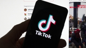 The TikTok logo is seen on a mobile phone in front of a computer screen which displays the TikTok home screen, Saturday, March 18, 2023, in Boston. THE CANADIAN PRESS/AP/Michael Dwyer