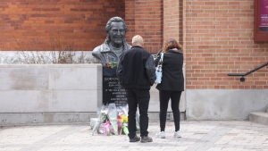 People stop to place flowers on the Gordon Lightfoot bust outside the Opera House in Orillia, Ont., on Tuesday, May 2, 2023. Tributes and condolences for the musical legend have been flowing since he passed away at 84 years old Monday May 1, 2023. THE CANADIAN PRESS/Christopher Drost