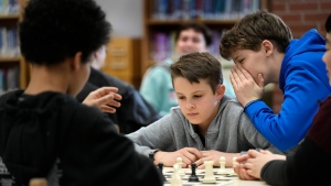 Owen Isenhour whispers advice to Eli Marquis during a Reeds Brook Middle School after-school chess practice, Tuesday, April 25, 2023, in Hampden, Maine. Part-time chess coach and full-time custodian David Bishop led his elementary and middle school teams to state championship titles this year. (AP Photo/Robert F. Bukaty)