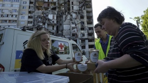 Local residents get free meals from volunteers against the background of their apartment house, damaged in the Russian rocket attack, in Kharkiv, Ukraine, Friday, June 2, 2023. (AP Photo/Andrii Marienko)
