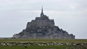 FILE - Sheeps graze in the fields around the Mont-Saint-Michel, Wednesday, May 8, 2018, in western France. France’s beloved abbey of Mont-Saint-Michel has reached a ripe old age. It's been 1,000 years since the laying of its first stone. The millennial of the UNESCO World Heritage site and key Normandy tourism magnet is being celebrated until November with exhibits, dance shows and concerts. French President Emmanuel Macron is heading there on Monday, June 5, 2023. (AP Photo/Thibault Camus, File)