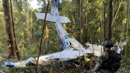 In this photo released by Colombia's Armed Forces Press Office, a soldier stands in front of the wreckage of a Cessna C206, Thursday, May 18, 2023, that crashed in the jungle of Solano in the Caqueta state of Colombia. A search continues for four Indigenous children who may have survived the deadly plane crash in the Amazon jungle on May 1. On Tuesday, May 16, soldiers found the wreckage and the bodies of three adults, including the pilot and the children's mother. (Colombia's Armed Forces Press Office via AP) 