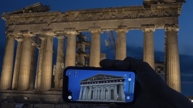 A woman holds up a mobile phone showing a digitally overlayed virtual reconstruction of the ancient Parthenon temple, at the Acropolis Hill in Athens, Greece on Tuesday, June 13, 2023. Greece has become a late but enthusiastic convert to new technology as a way of displaying its famous archaeological monuments and deepening visitors' knowledge of ancient history. The latest virtual tour on offer is provided by a mobile app that uses Augmented Reality to produce digital overlays that show visitors at the Acropolis how the site and its sculptures looked 2,500 ago. (AP Photo/Petros Giannakouris)