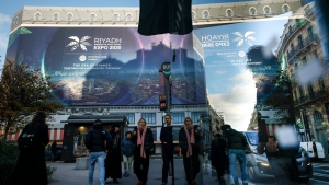People walk by a building under renovation protected with a canvas decorated with a commercial promoting the Riyadh Expo 2030, Tuesday, Nov. 28, 2023 in Paris. In a high-profile showdown, Rome, Busan and Riyadh are the top contenders to become the host city of the 2030 World Expo, with the organizing body choosing the winner on Tuesday. (AP Photo/Thomas Padilla)