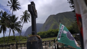 Flags blow in the breeze at the grave of Father Damien outside St. Philomena Church on Kalaupapa, Hawaii, on Tuesday, July 18, 2023. Damien was canonized a Catholic saint in 2009 for his work taking care of the physical and spiritual needs of leprosy patients in the 1800s. His body was moved to his home country of Belgium in 1936. Only the priest's hand remains, which was reburied at the site in 1995. (AP Photo/Jessie Wardarski)