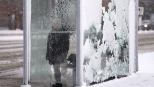 A person huddles in a bus shelter as they wait for public transit as winter storm moves in swathes of Ontario, in Toronto, Tuesday, Jan. 9, 2024. THE CANADIAN PRESS/Chris Young