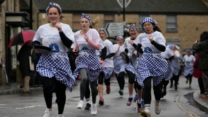 Competitors run ahead during the annual Shrove Tuesday trans-Atlantic pancake race in the town of Olney, in Buckinghamshire, England, Tuesday, Feb. 13, 2024. Every year women clad in aprons and head scarves from Olney and the city of Liberal, in Kansas, USA, run their respective legs of the race with pancakes in their pans. According to legend, the Olney race started in 1445 when a harried housewife arrived at church on Shrove Tuesday still clutching her frying pan with a pancake in it. (AP Photo/Kin Cheung)