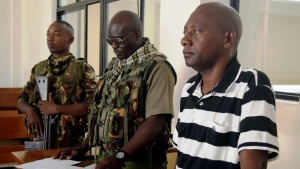 Cult preacher Pastor Paul Nthenge Mackenzie, right, stands at the Malindi Law Courts under tight security, Friday Dec. 1, 2023 for the sentencing of his 2019 case where he had been charged with three counts of being in possession of films intended to incite children against attending school and incite Christians, Hindus, Buddhists and Islams on their religion. (AP Photo/Gideon Maundu)
