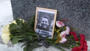This grab taken from video shows flowers and a portrait of Russian opposition leader Alexei Navalny that Lyudmila Navalnaya, mother of Russian opposition leader Alexei Navalny, put to pay tribute to her son at the at the memorial to victims of political repression, in Salekhard, 1937 km (1211 miles) northeast of Moscow, Russia, on Tuesday, Feb. 20, 2024. (AP Photo)