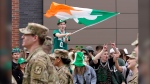 FILE - A spectator, top, waves a flag that features a likeness of a shamrock as members of the Boston University ROTC program, left, march past during the St. Patrick's Day parade, Sunday, March 20, 2022, in Boston's South Boston neighborhood. The day honoring the patron saint of Ireland is a global celebration of Irish heritage. And nowhere is that more so than in the United States, where parades take place in cities around the country and all kinds of foods and drinks are given an emerald hue. (AP Photo/Steven Senne, File)