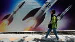 A woman walks past a banner showing missiles being launched, in northern Tehran, Iran, Friday, April 19, 2024. Iran fired air defenses at a major air base and a nuclear site near the central city of Isfahan after spotting drones early Friday morning, raising fears of a possible Israeli strike in retaliation for Tehran's unprecedented drone-and-missile assault on the country. On the missiles, a decorative sign reads: "Allah" (AP Photo/Vahid Salemi)