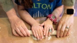 Wearing a necklace with her name in Hebrew, Charlotte Gleicher, 7, a first grader at Milton Gottesman Jewish Day School of the Nation's Capital, is helped by her teacher, Dafna Kiverstein, to roll out dough for matzah during a "Matzah Factory" field trip at the JCrafts Center for Jewish Life and Tradition in Rockville, Md., Thursday, April 18, 2024, ahead of the Passover holiday.(AP Photo/Jacquelyn Martin)