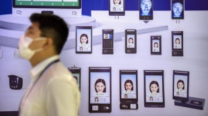 A visitor wearing a face mask walks past a billboard from a firm advertising its AI facial recognition technology at the PT Expo in Beijing, Sunday, June 4, 2023. Travellers in Canada would be able to use facial recognition technology to identify themselves through their smartphones when crossing the border under a planned federal project. THE CANADIAN PRESS/AP-Mark Schiefelbein