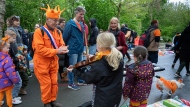 An orange-clad man applauds for a girl playing violin as his orange-clad dog, bottom right corner, runs off during King's Day celebrations in Amsterdam, Netherlands, Saturday, April 27, 2024. (AP Photo/Peter Dejong)