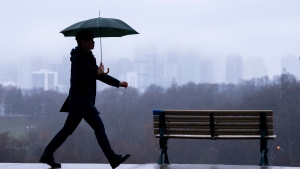 The Toronto skyline sits shrouded in fog as a man walks in the rain on Thursday December 28, 2023. THE CANADIAN PRESS/Frank Gunn