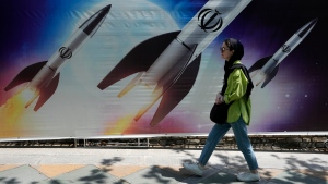 A woman walks past a banner showing missiles being launched, in northern Tehran, Iran, Friday, April 19, 2024. (AP Photo/Vahid Salemi) 