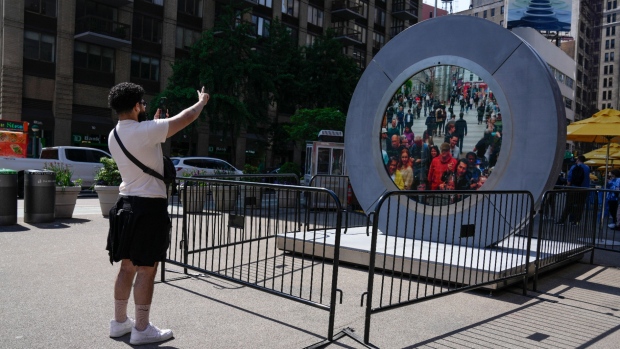 A man signals to pedestrians in Dublin, Ireland, through a livestream portal as part of an art installation on the street in New York, May 14, 2024. (AP Photo/Seth Wenig)