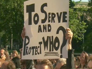 A protester holds up a sign saying 'To Serve and Protect Who?' at a rally on Thursday, July 1, 2010 to demand an inquiry into police conduct during the G20 Summit in Toronto.