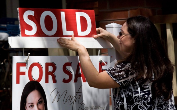 A real estate agent puts up a 'sold' sign in front of a house in Toronto