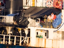 Migrants, right, look over the side of the MV Sun Sea while armed police officiers stand by after the ship was escorted into CFB Esquimalt in Colwood, B.C.,Friday, Aug. 13, 2010. (THE CANADIAN PRESS/Jonathan Hayward)