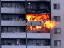 A resident looks up as flames shoot from a 24th floor apartment Friday afternoon. (CP24 MyBreakingNews - Jeff Riffle)