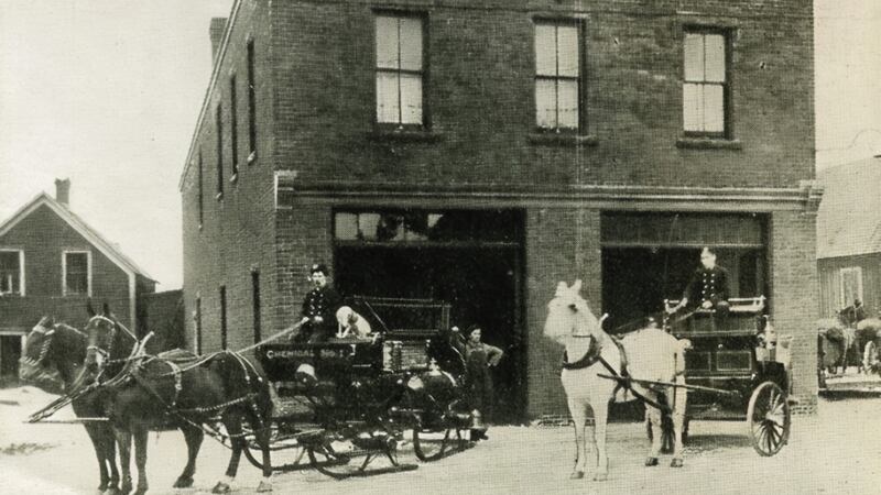Firefighters are pictured with horses in a black and white photo.
