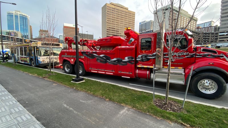 A large tow truck has a transit bus attached to the back.