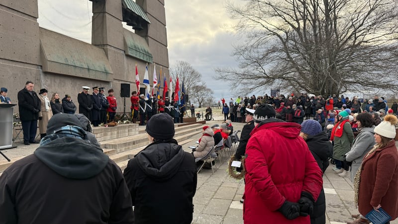 People wearing winter clothing stand in front of a stone monument.
