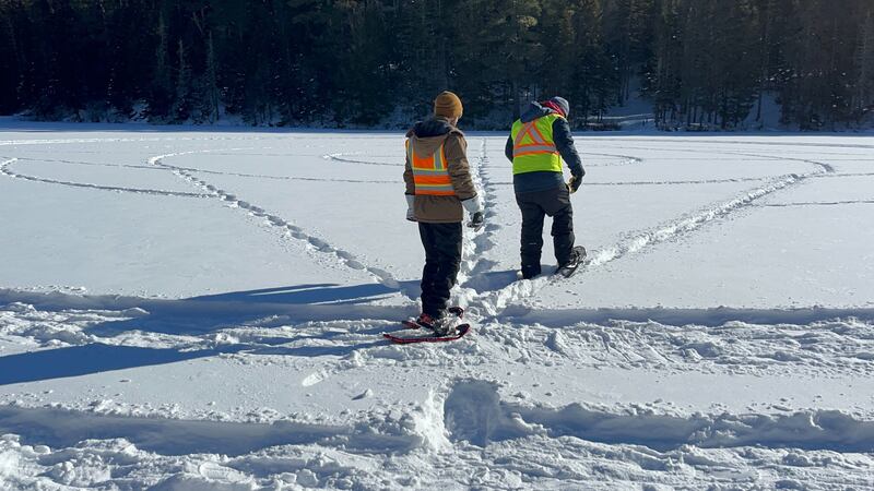 Two men walk on a frozen lake covered in snow.
