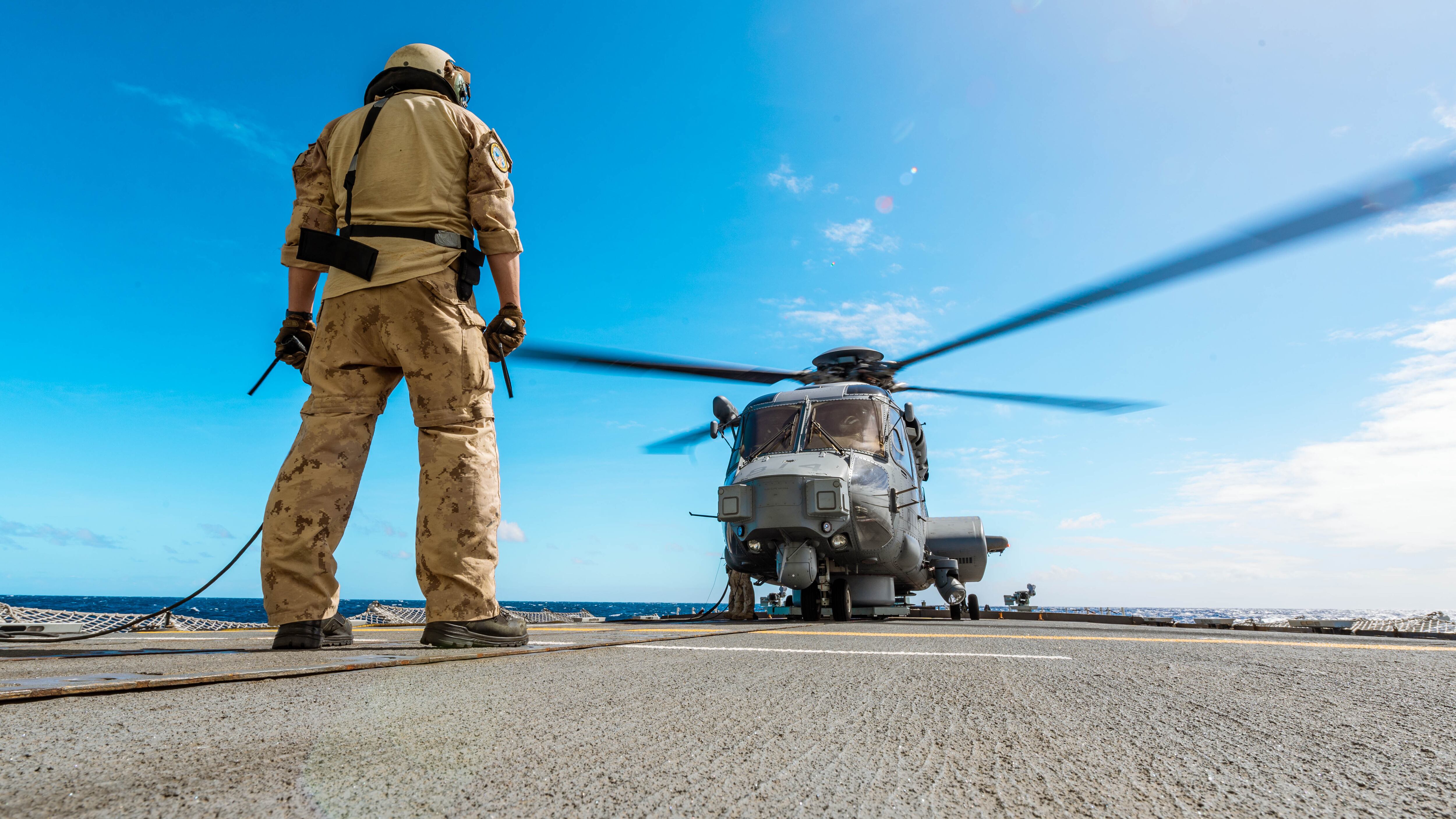 Joshua Streeter, an air weapons technician onboard HMCS Montreal, stands in front of the ship's embarked CH-148 Cyclone helicopter as part of Exercise Talisman Sabre on July 27, 2023. (Cpl. Connor Bennett/The Canadian Armed Forces)