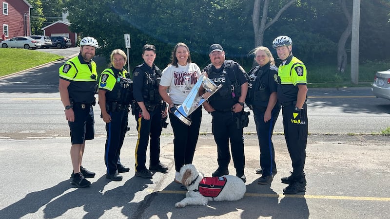 A group of first responders pose for a photo with a hockey coach and trophy.