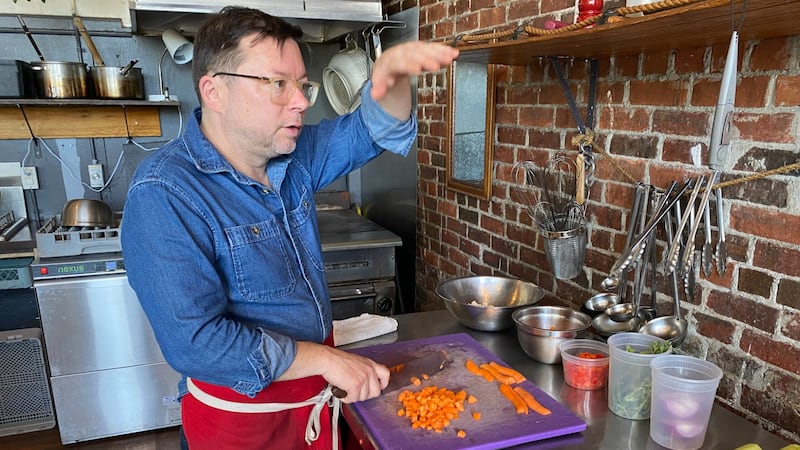 A man in a blue denim shirt chops carrots.