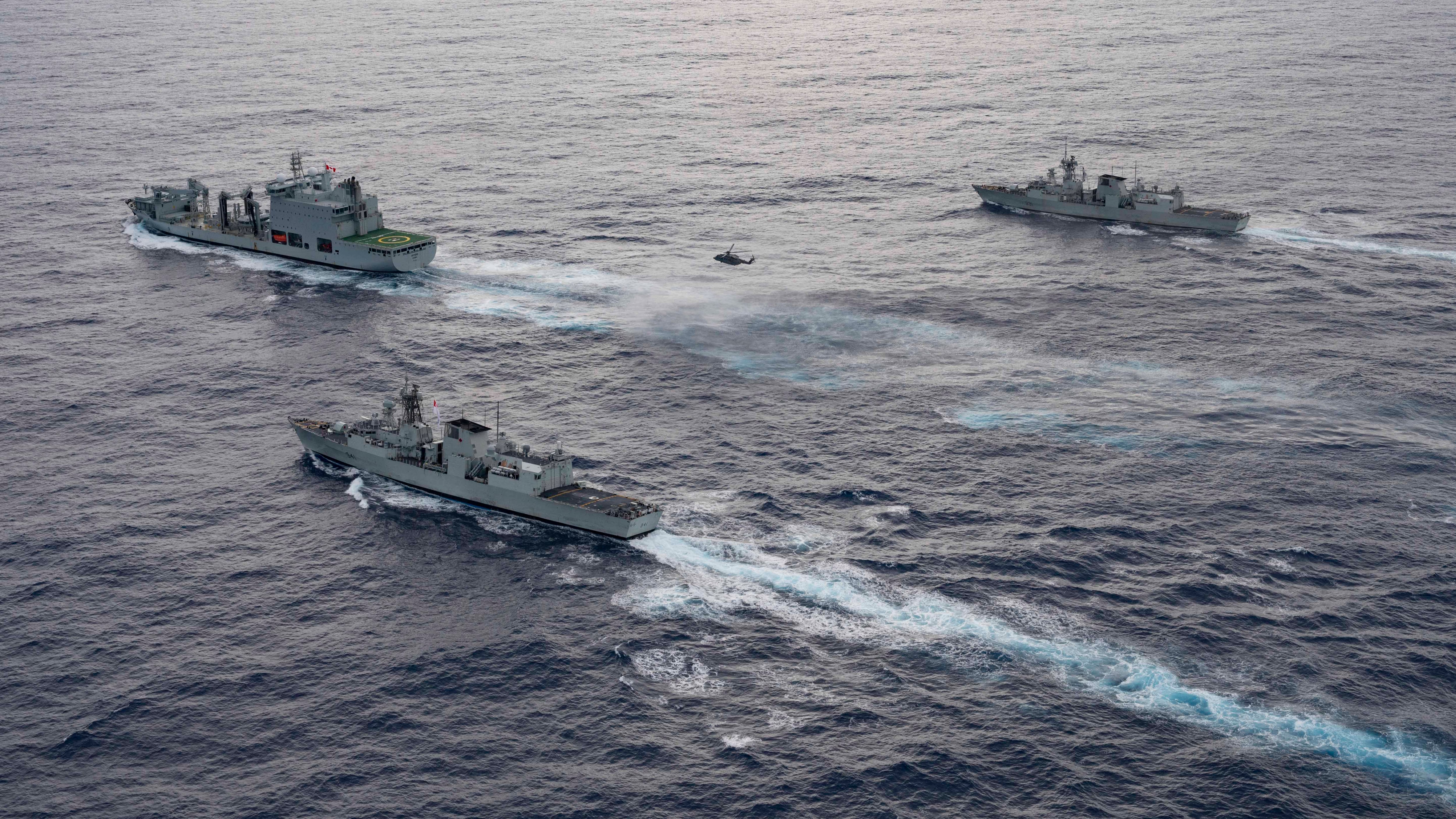 From front to back, HMCS Ottawa and its embarked CH-148 Cyclone helicopter, supply vessel Asterix and HMCS Vancouver, take part in a photo exercise in the Pacific Ocean on Dec. 1, 2023.