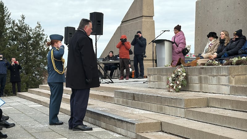 People stand in front of a wreath which has been placed on a stone monument.